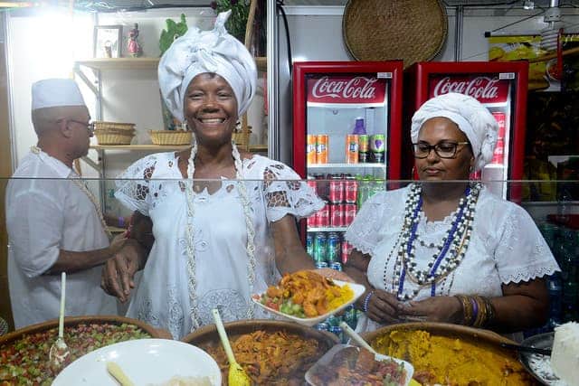 Imagem de uma baiana vendendo acarajé no estande da Praça
