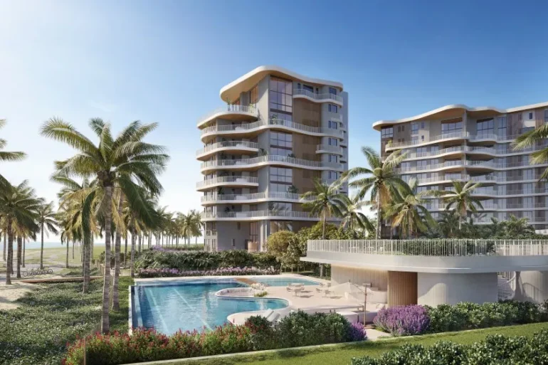 Renderização de dois edifícios residenciais com varandas curvas e fachada bege, cercados por palmeiras, jardins e piscina à beira-mar.